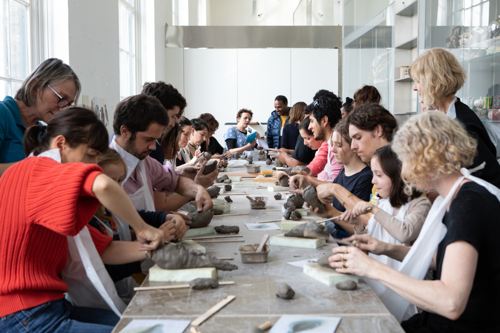 People sit at a long table working clay with their hands